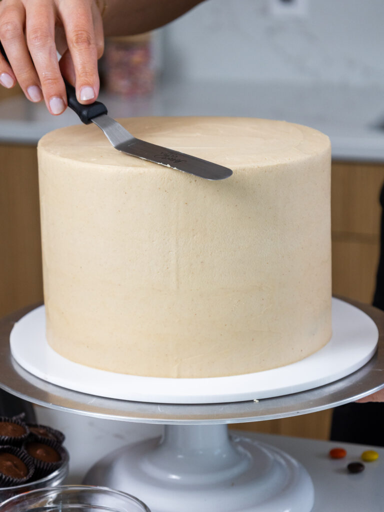 image of peanut butter buttercream frosting being smoothed onto a reese's cake