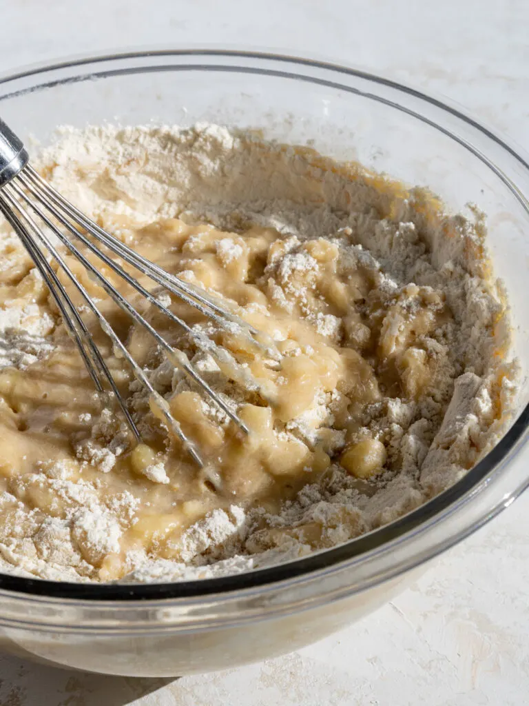 image of banana muffin batter being whisked together in a glass bowl