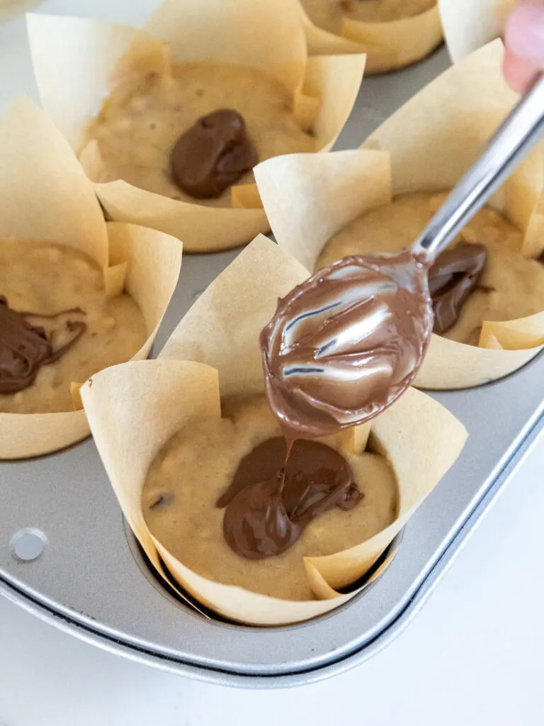 image of nutella being scooped into the center of a nutella banana muffin
