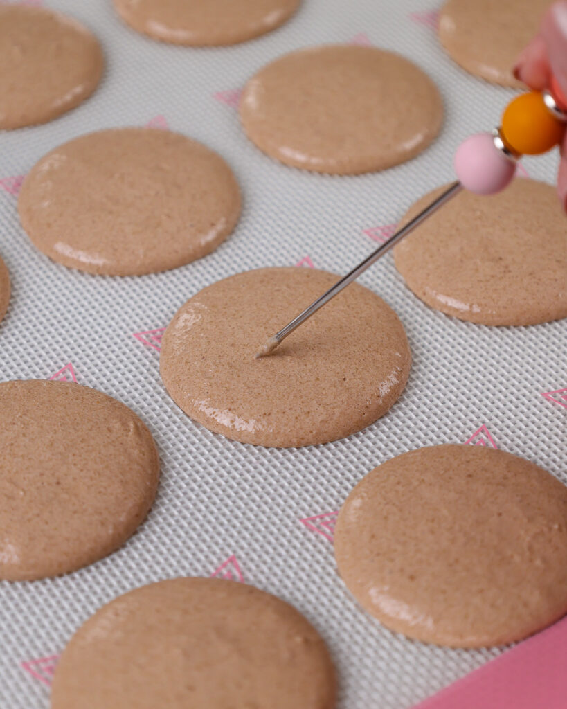 image of chocolate macaron shells that are having their bubbles popped with a scribe