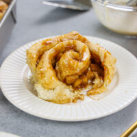 image of caramel apple cinnamon roll being topped with caramel drizzle