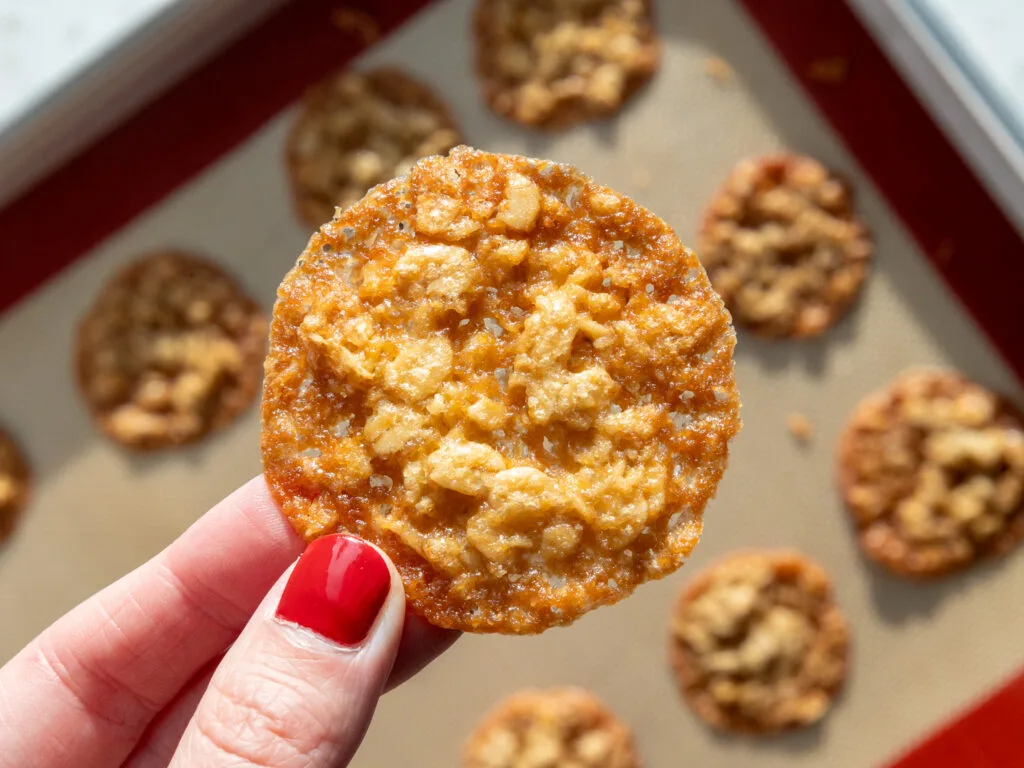 image of an oatmeal lace cookie being held up in the sunshine to show how perfectly caramelized it is