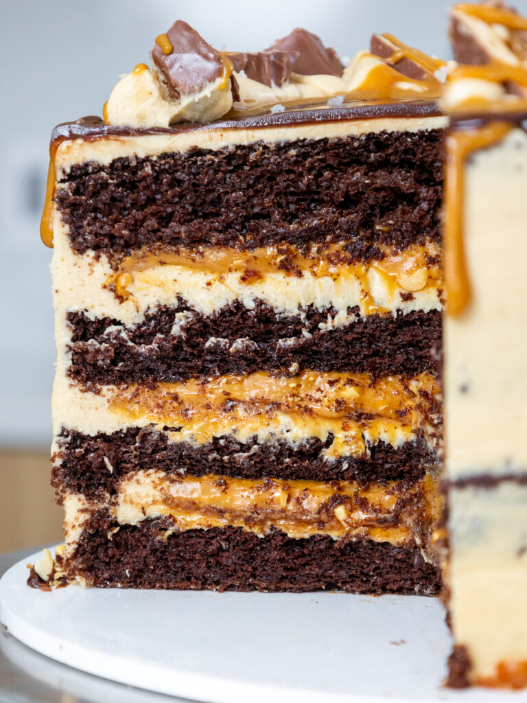 image of a snickers cake that's been cut into to show it's peanut caramel filling and peanut butter buttercream