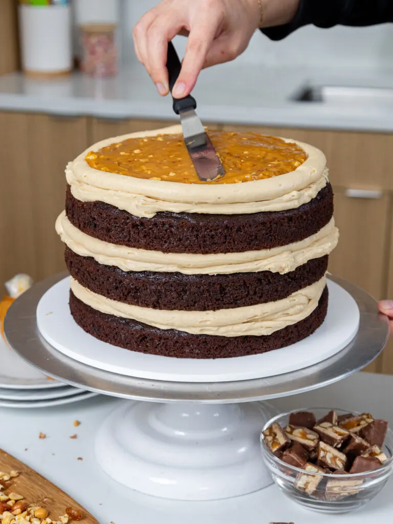 image of a chocolate snickers cake being filled with peanut buttercream and a thick peanut caramel