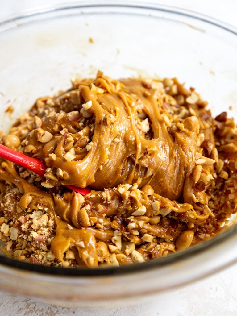 image of chopped peanuts being folded into whipped caramel to make the filling for a snickers cake