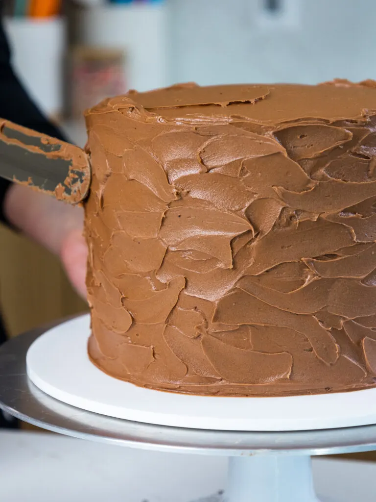 image of Nutella buttercream being swirled around a Nutella cake with a large offset spatula