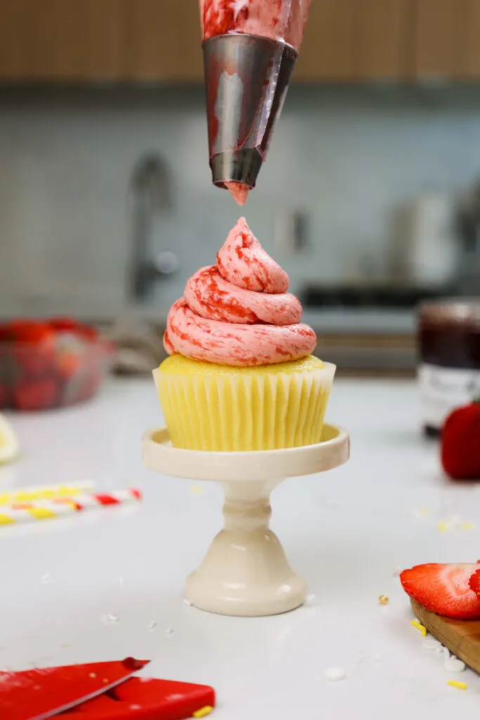 image of strawberry buttercream made with jam being piped onto a lemon cupcake