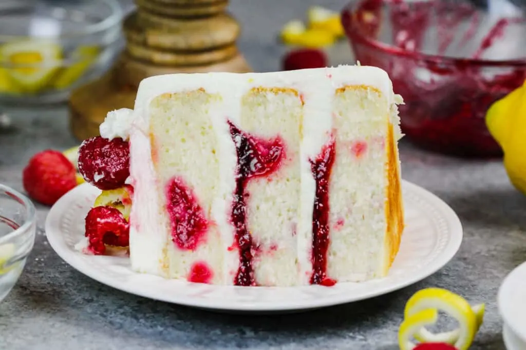 image of a slice of lemon rapsberry cake on a plate, showing it's raspberry filling and lemon cream cheese frosting