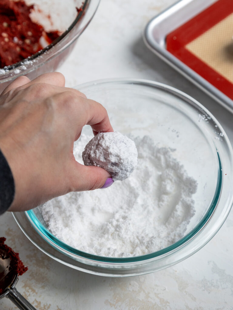 image of a red velvet crinkle cookie being tossed in powdered sugar