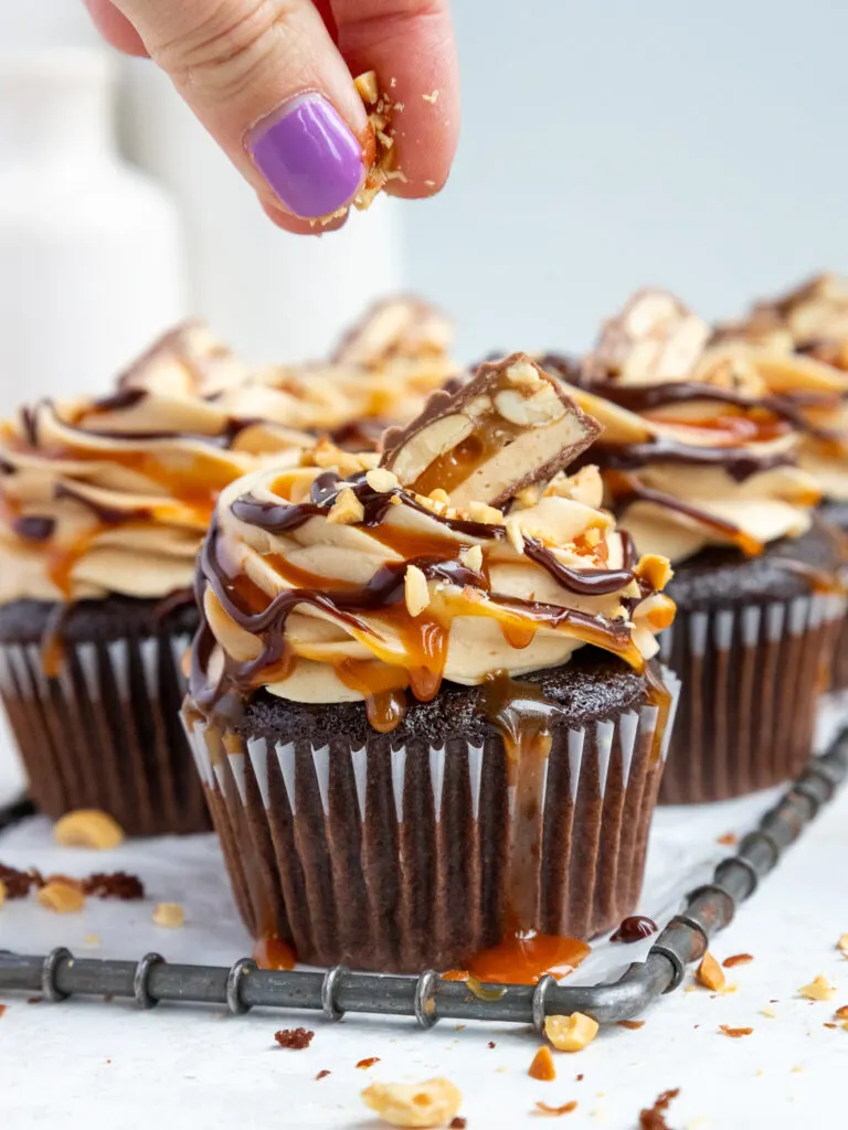 image of chopped peanuts being sprinkled on a snickers cupcake