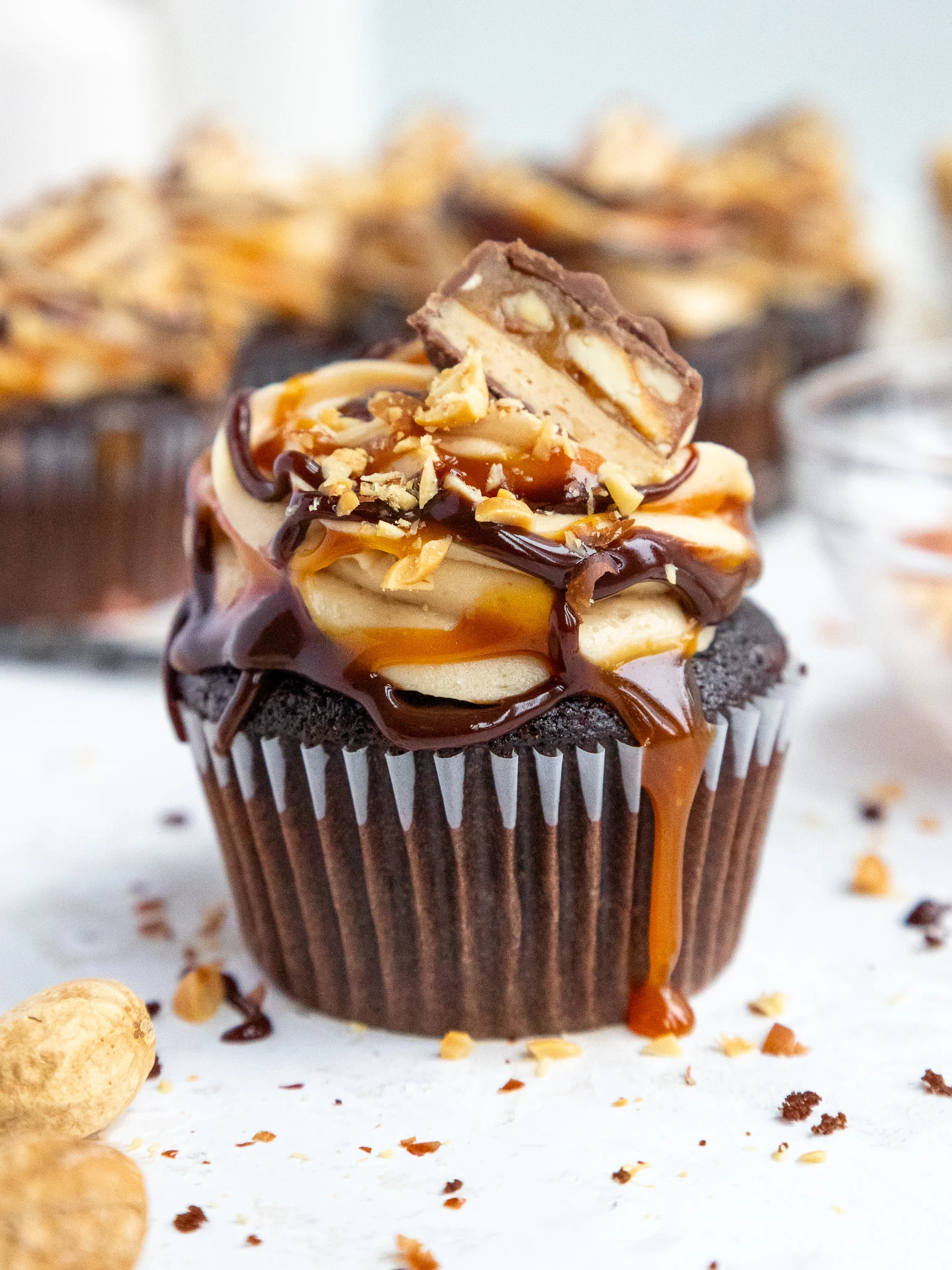 image of a snickers cupcake that's been decorated with peanut butter buttercream and caramel and chocolate ganache