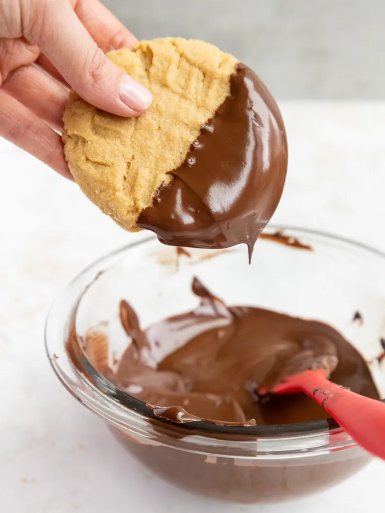 image of a peanut butter cookie being dipped in melted chocolate