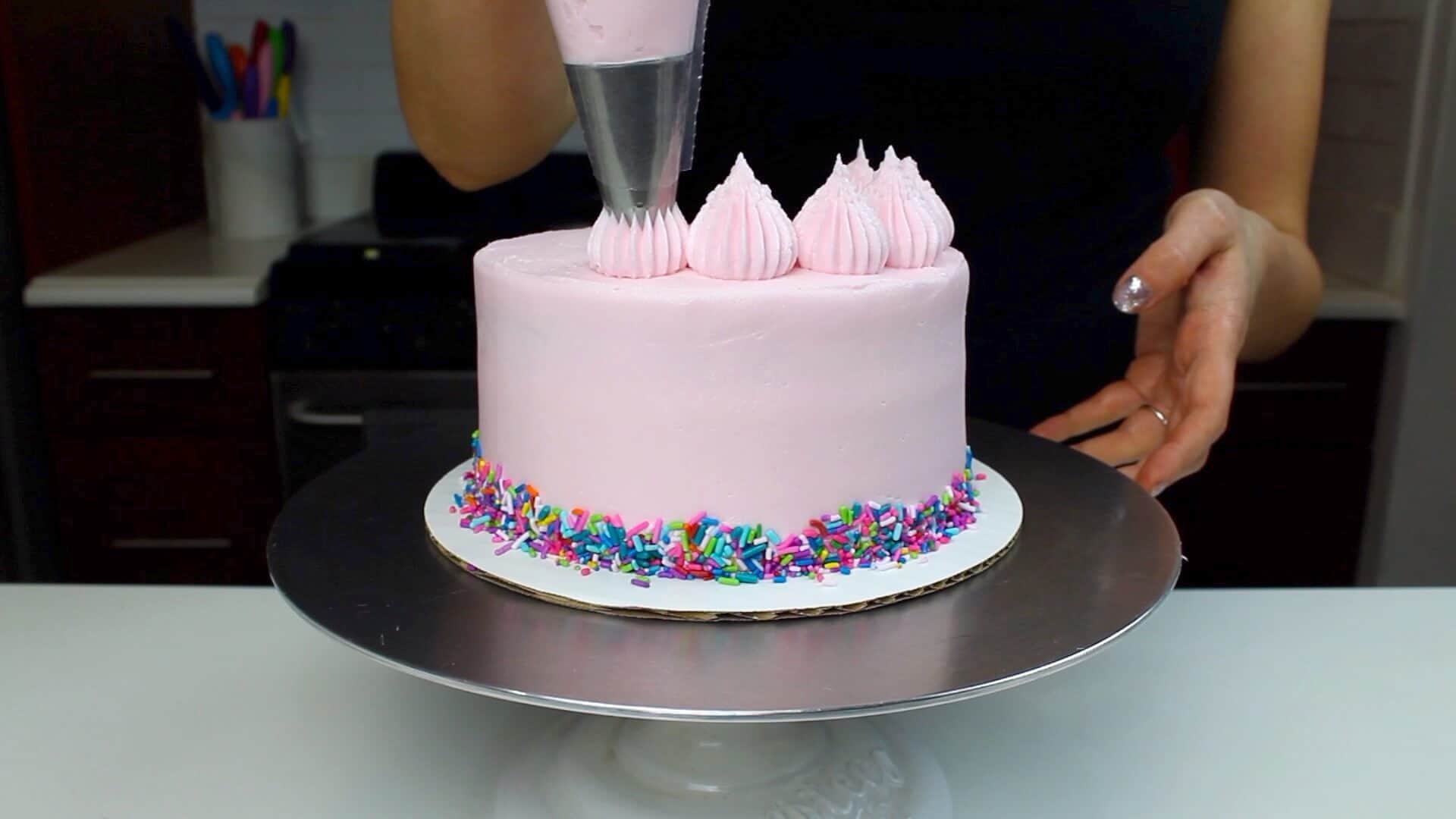 image of adding frosting border to the top of a pink vegan layer cake