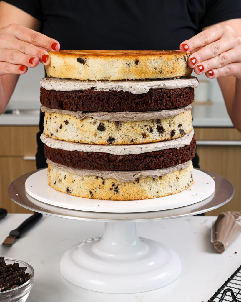 image of oreo cake layers and brownie cake layers being stacked with oreo buttercream frosting