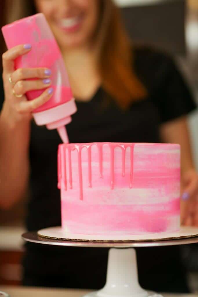 Adding pink drips to a vanilla layer cake using a squirt bottle
