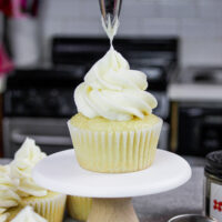 image of vanilla American buttercream being piped onto a fluffy vanilla cupcake
