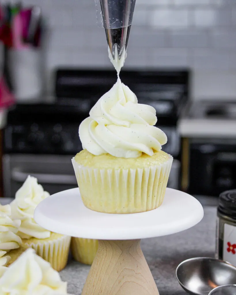 image of vanilla American buttercream being piped onto a fluffy vanilla cupcake