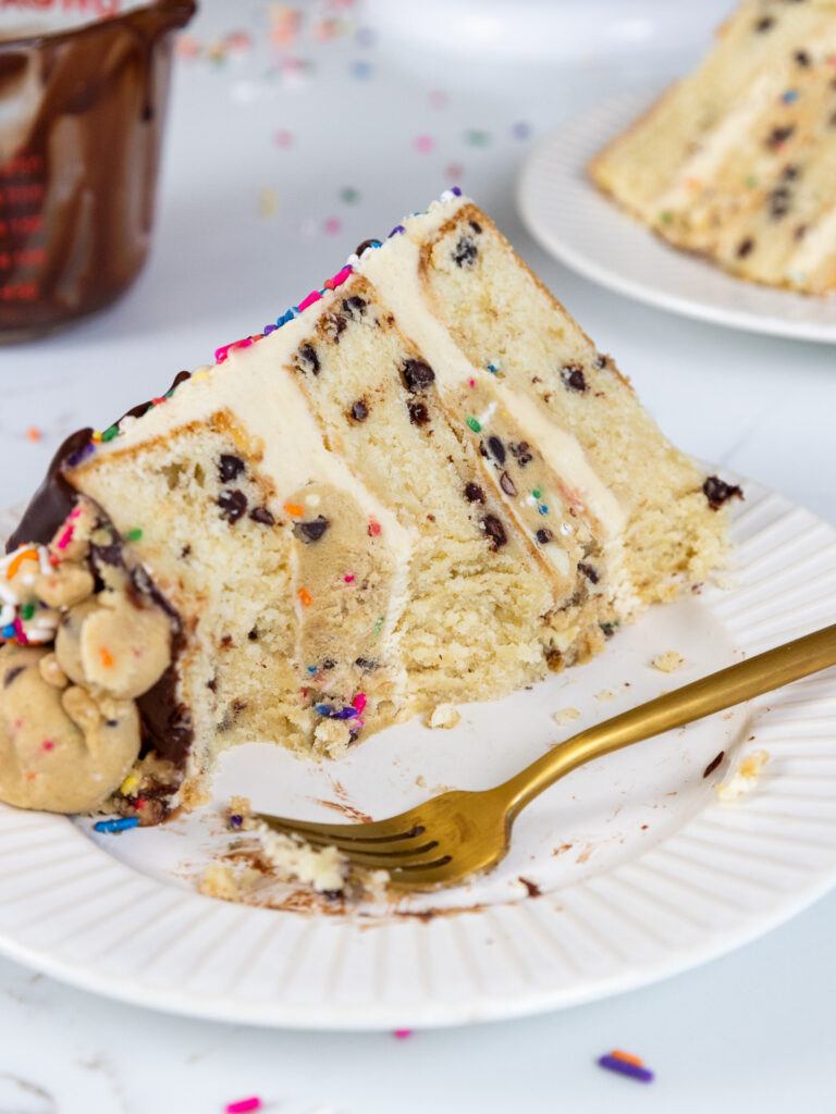 image of a slice of cookie dough cake that's on a plate and has been cut into to show how tender the cake layers are and how delicious the cookie dough cake filling is
