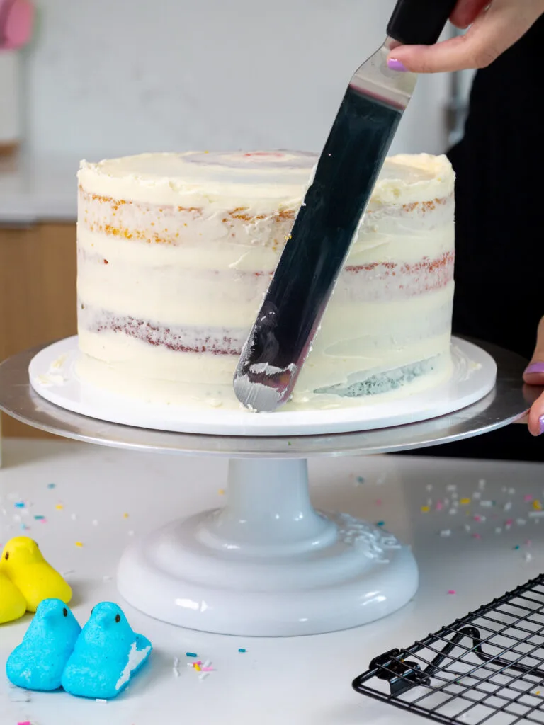 image of a peeps cake that's being crumb coated with a thin layer of frosting using a large offset spatula