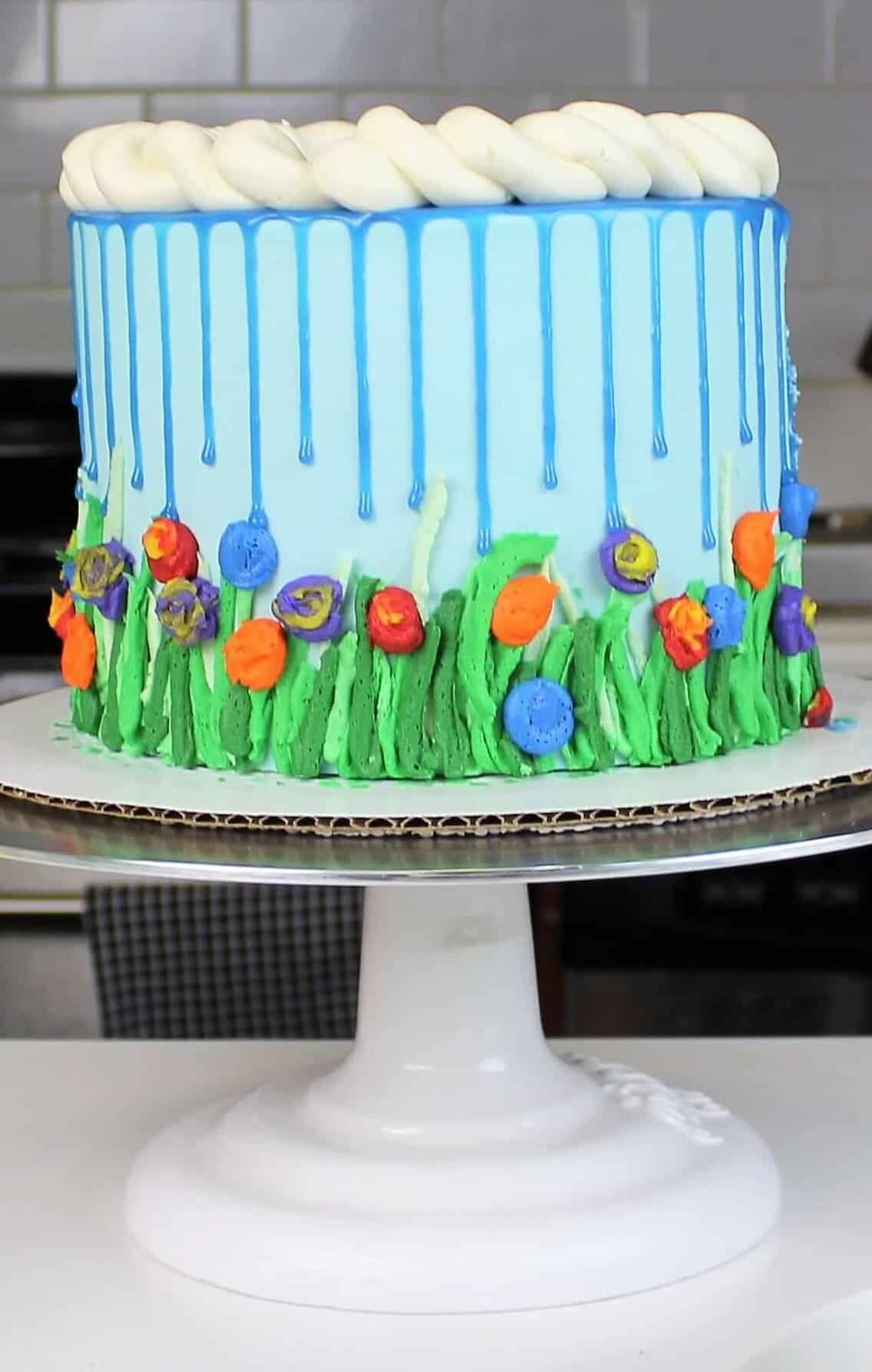 Spring themed cake, decorated with blue drips and colorful buttercream flowers to represent April showers