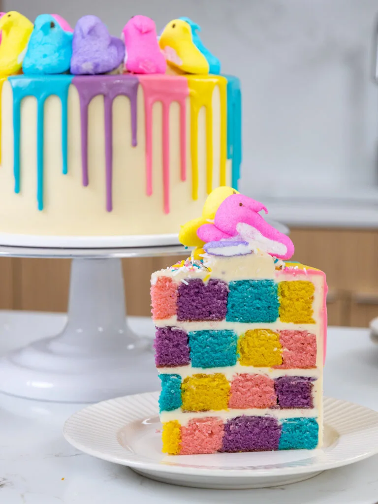 image of a cute Easter checkerboard cake slice on a plate in front of a Peeps drip cake