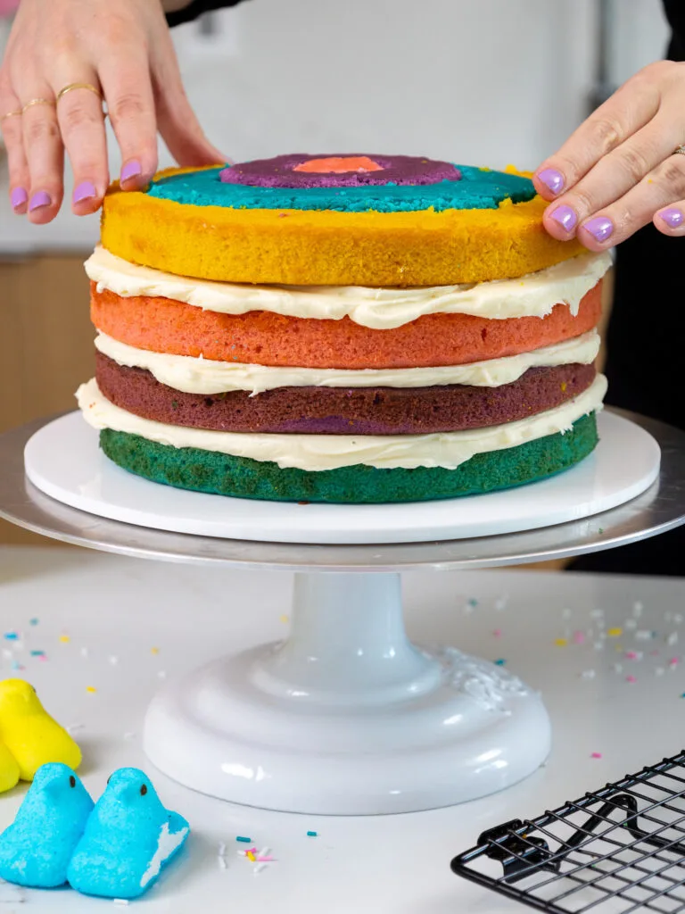 image of checkerboard cake layers being stacked and filled with buttercream frosting