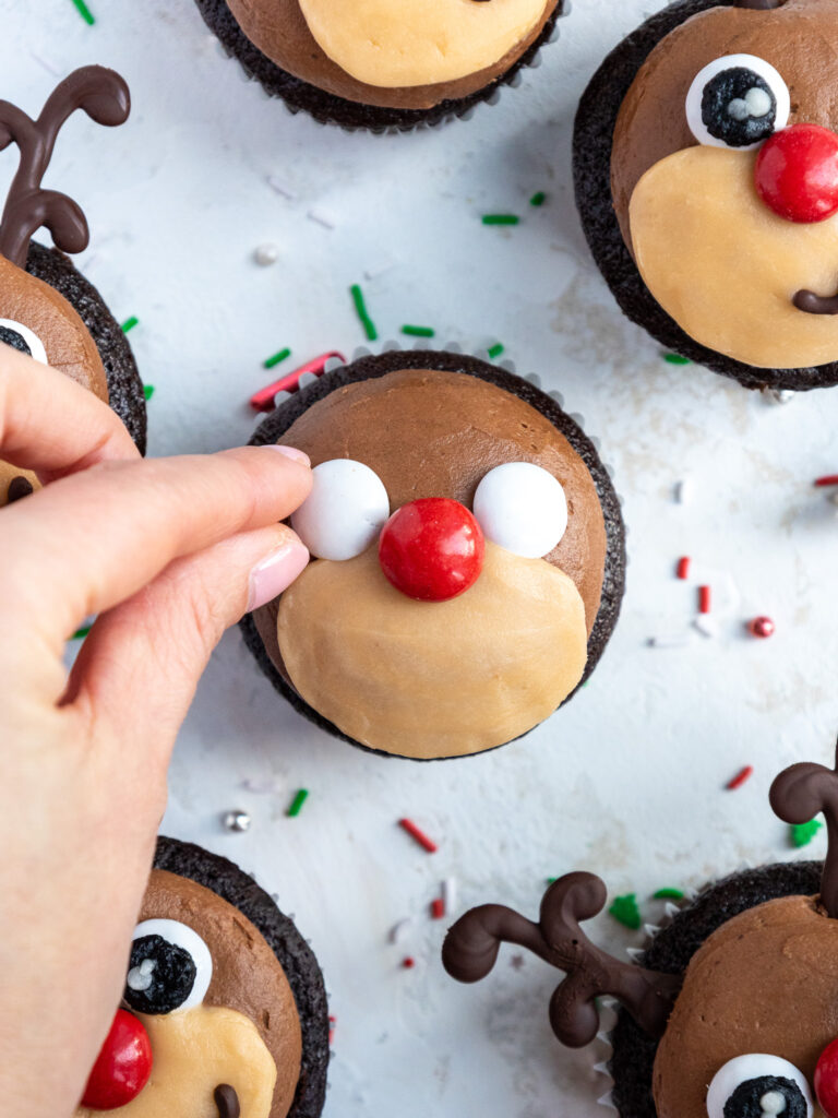 image of white and red M&Ms being added onto a reindeer cupcake