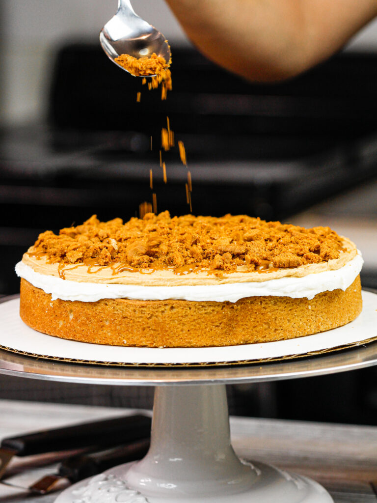 image of biscoff cookies being sprinkled between the layers of a biscoff cake