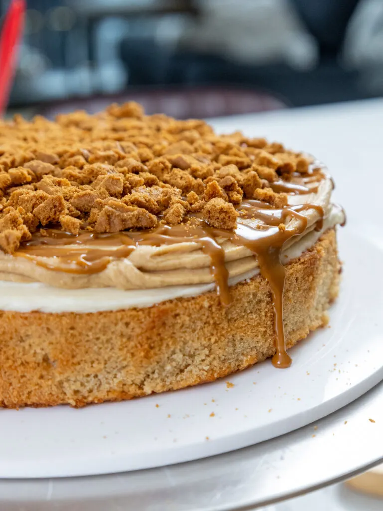 image of a lotus cake being assembled with biscoff cake layers, cookie butter frosting, and a cookie butter drizzle
