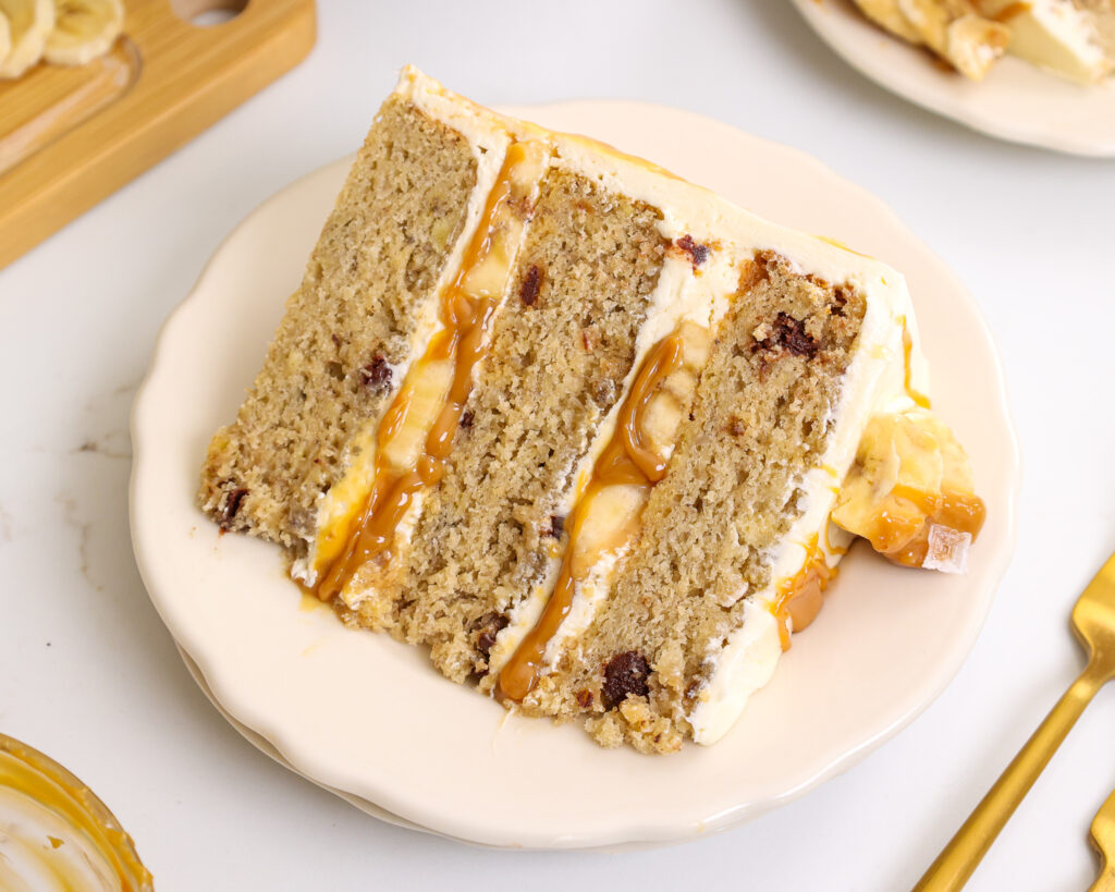 image of a slice of banoffee cake on a plate that's made with banana cake layers, toffee and fresh banana slices
