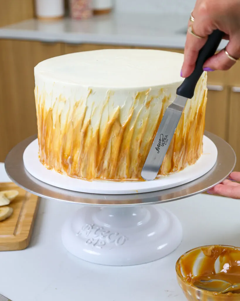 image of toffee being spread up the side of a banoffee layer cake to decorate it