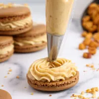 image of peanut butter frosting being piped onto a macaron shell