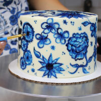 image of a painted buttercream cake decorated with hand painted blue flowers using gel food coloring and vodka to make edible paint