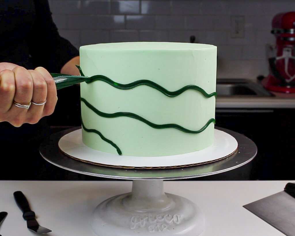 image of dark green frosting being piped around a cake to make it look like it's decorated with Christmas lights