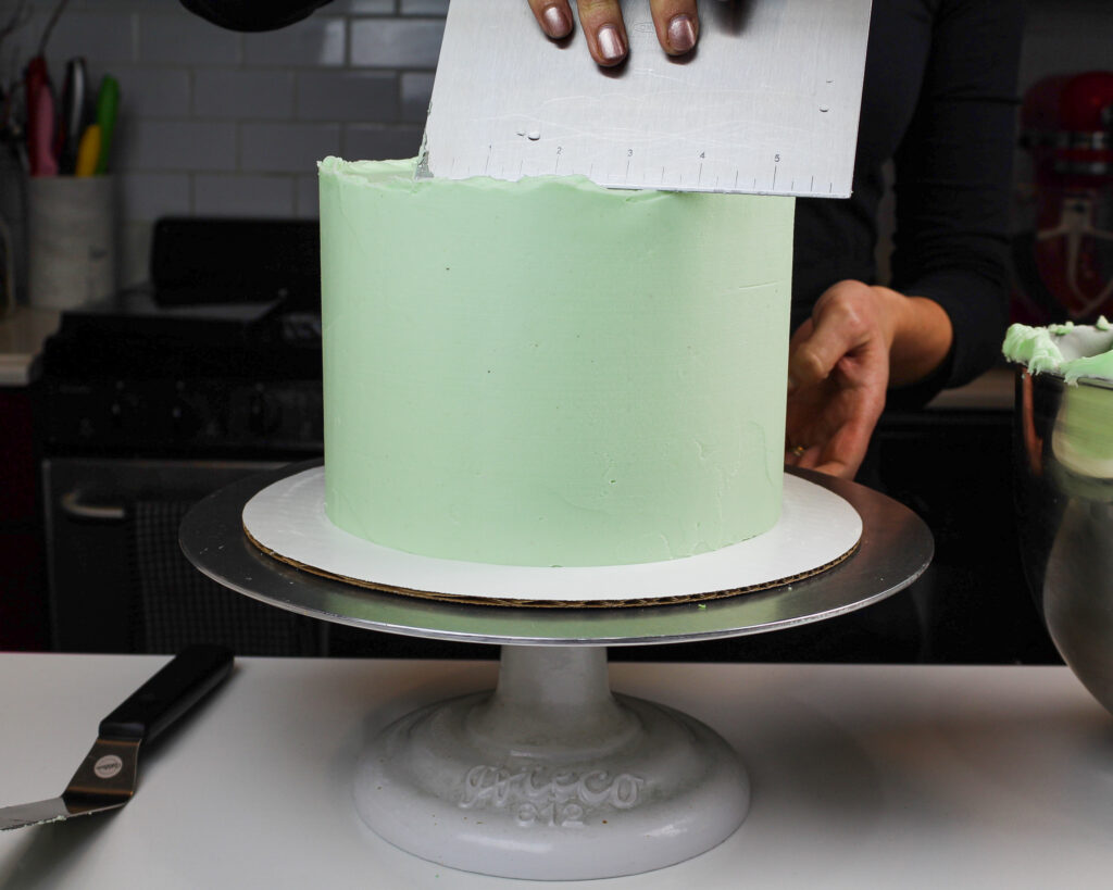 image of a cake being frosted with light green colored buttercream frosting