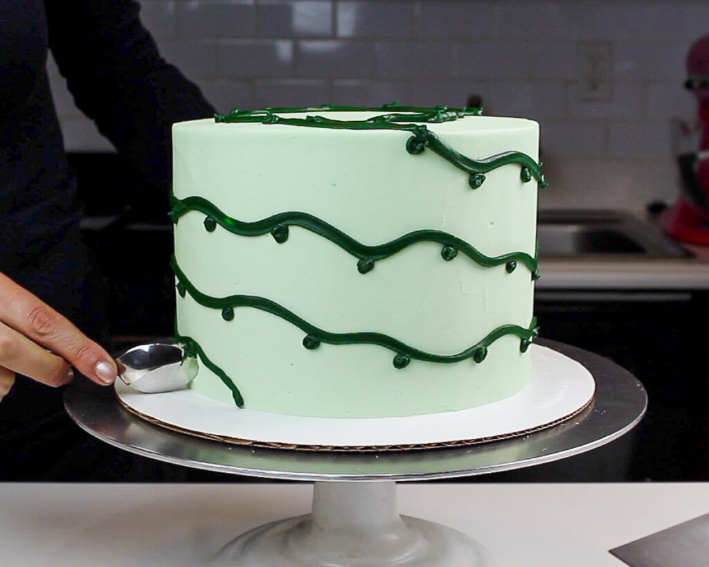 image of dark green frosting being piped around a cake to make it look like it's decorated with Christmas lights