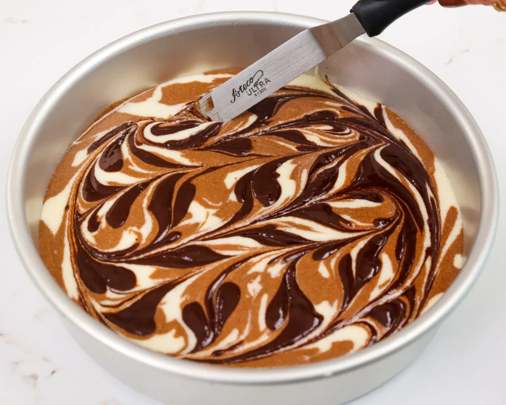 image of chocolate and vanilla cake batter being swirled together to make marble cake layers