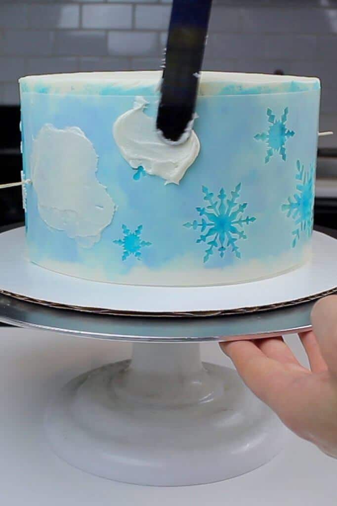 Adding buttercream snowflakes onto my snowflake cake using a cake stencil! Such an easy and fun cake decorating technique!!