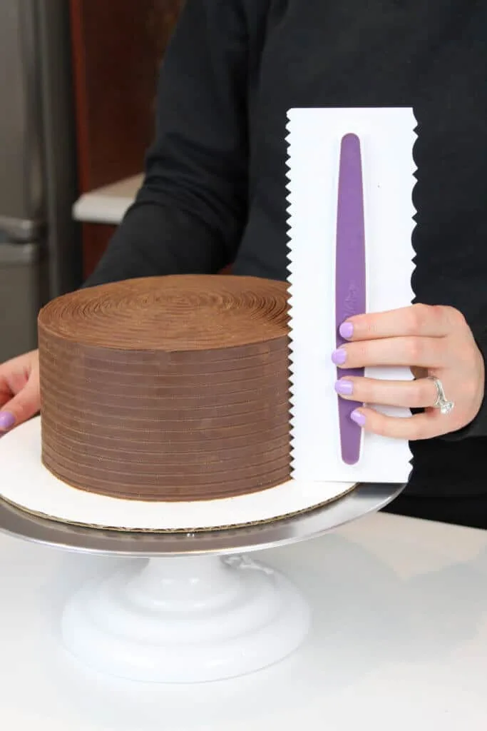using an icing comb to smooth ganache onto a cake