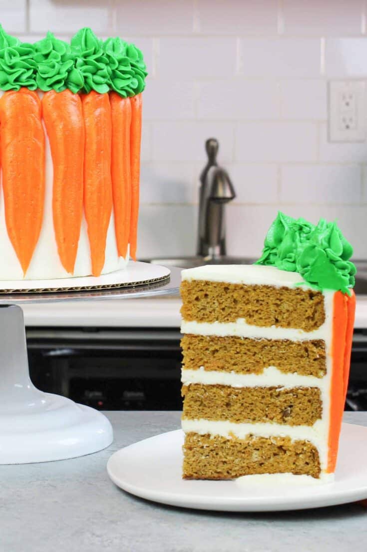 carrot cake slice frosted with cream cheese buttercream, with decorated carrot cake in background