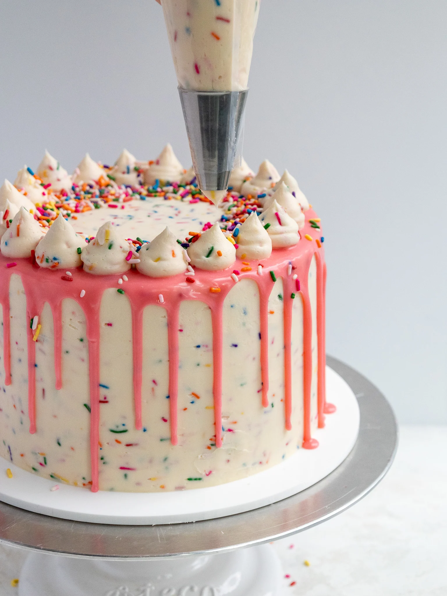 image of sprinkle funfetti buttercream being piped in a ring on top of a funfetti cake
