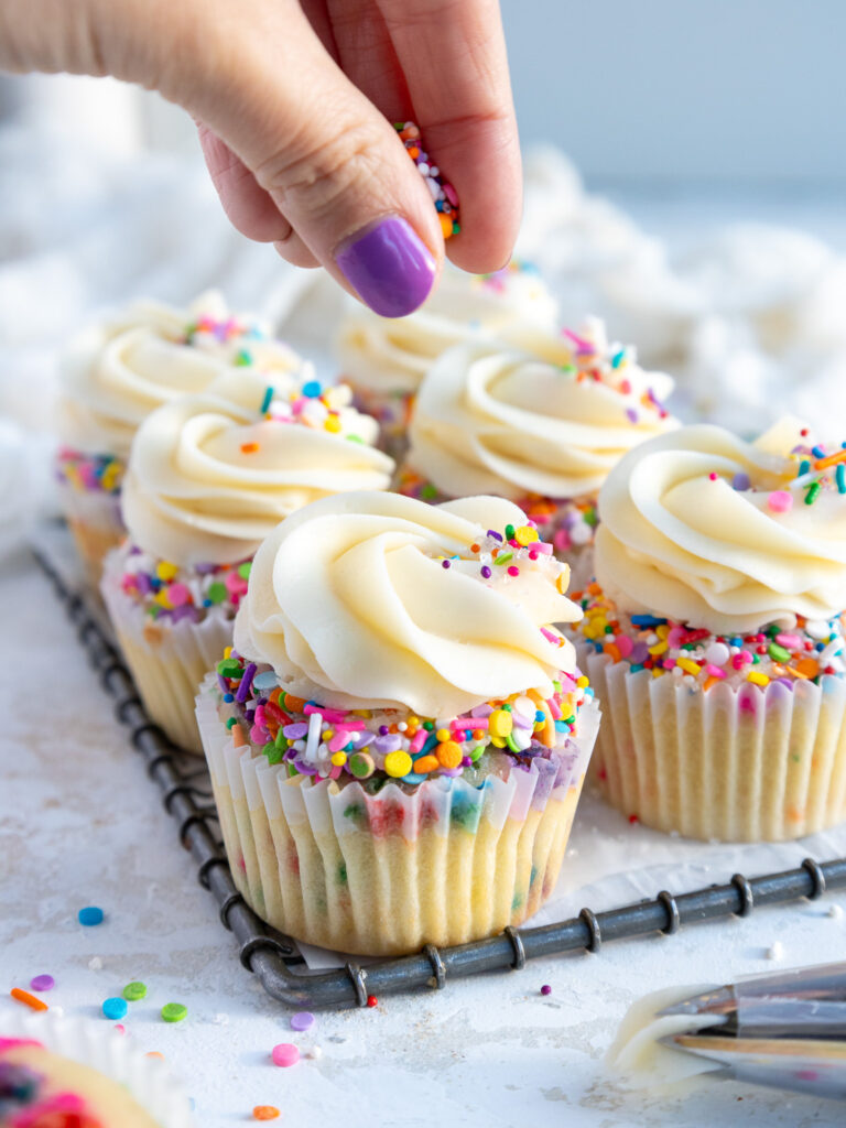 image of rainbow sprinkles being added as a garnish to the top of funfetti cupcakes