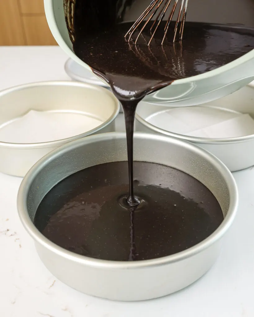 image of a black velvet cake batter being poured into a round cake pan