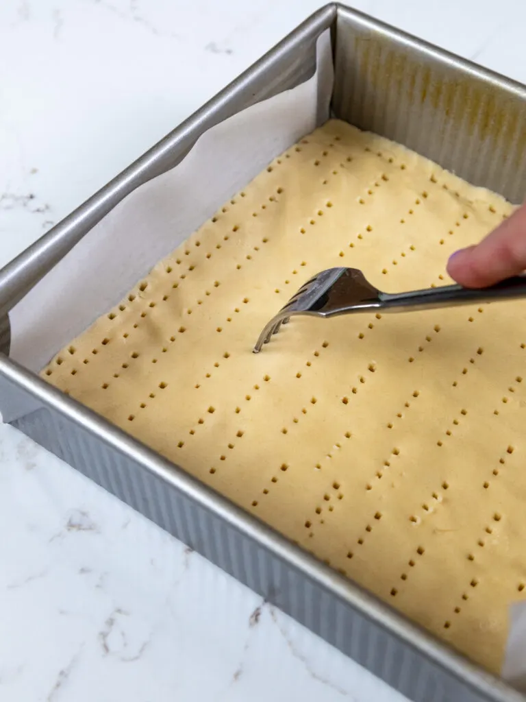 image of a shortbread crust being poked with holes using a fork before being baked