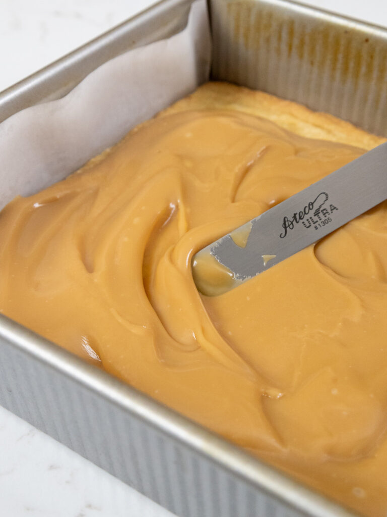 image of caramel being spread over a shortbread crust to make millionaire bars