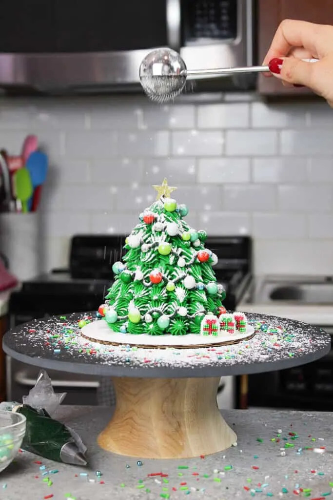 image of adding powdered sugar snow to christmas tree cake using a dusting wand that's included in a list of gifts for bakers 2020
