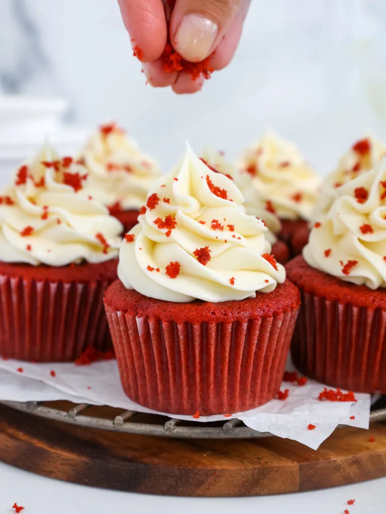 image of red velvet cake crumbs being sprinkled on top of a moist red velvet cupcake