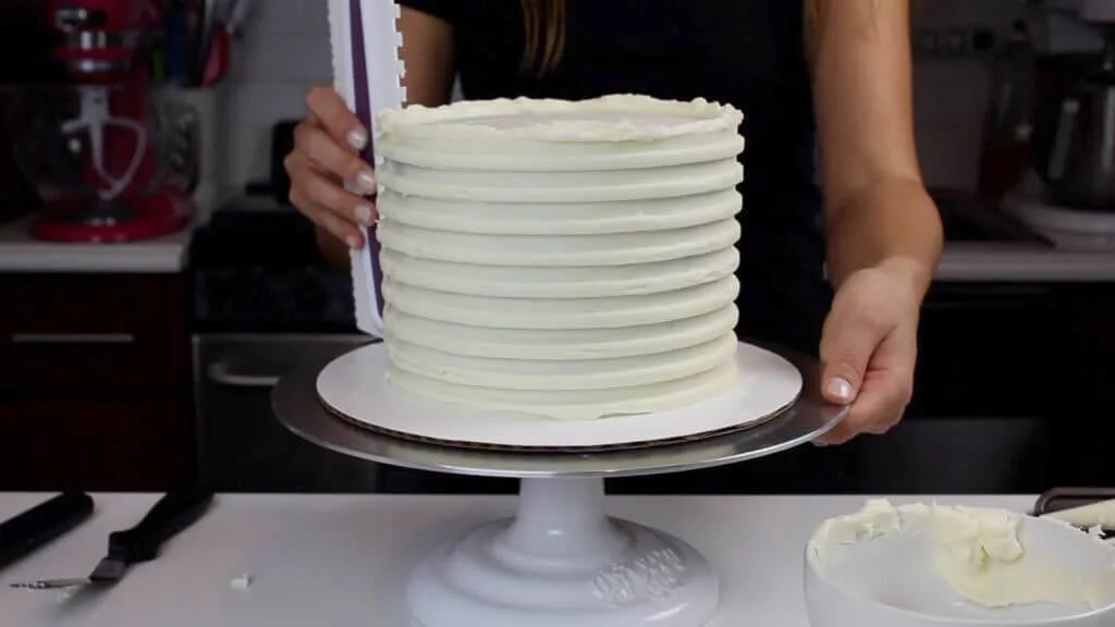 image of icing comb being used to create grooves for a striped buttercream cake