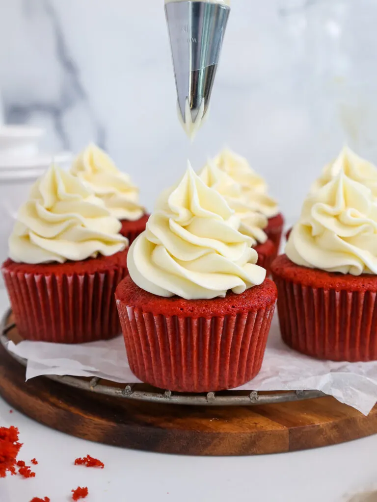 image of cream cheese buttercream frosting being piped onto a red velvet cupcake with a wilton 1m frosting tip