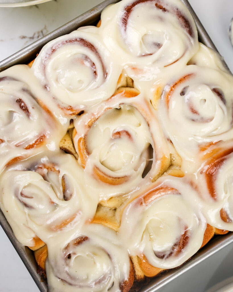 image of cream cheese frosting being added to cinnamon rolls